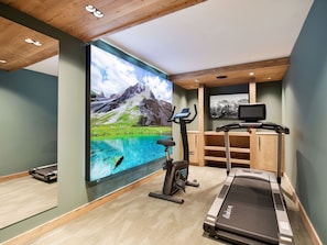 A home gym with a treadmill, stationary bike, and a large wall-mounted TV displaying a scenic mountain landscape. - Chalet at the slopes - 12 guests (Méribel Village)