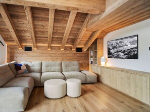 Une pièce chaleureuse avec un plafond en bois, un canapé d’angle et un tableau accroché au mur.