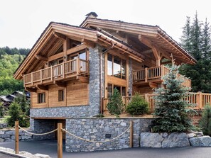 A wooden chalet with a stone foundation, wooden balconies, and a stone retaining wall. - Chalet at the slopes - 12 guests (Méribel Village)
