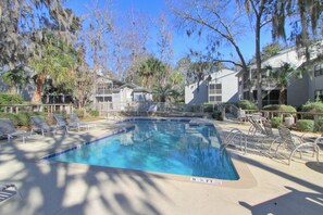 A swimming pool with lounge chairs, surrounded by trees and buildings. - 22 Ocean Breeze: 3 Bedrooms, Hosts 6, Walk to Beach! (Hilton Head Island)