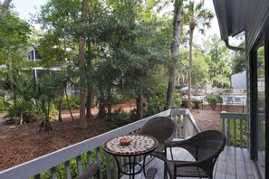 A covered outdoor area with a table and chairs, surrounded by trees and a pool. - 22 Ocean Breeze: 3 Bedrooms, Hosts 6, Walk to Beach! (Hilton Head Island)