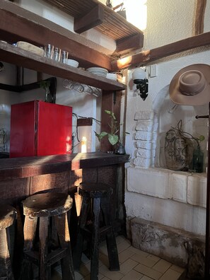 A rustic kitchen with a red refrigerator, wooden stools, and a brick wall with decorative items.