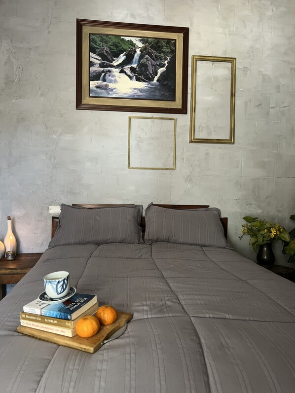 A bedroom with a bed, pillows, a framed picture, a bedside table with a lamp, and a vase with flowers.