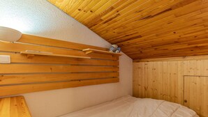 Une chambre avec une tête de lit en lattes de bois, un lit recouvert d’une couette blanche et une petite étagère sur laquelle est posé un ours en peluche.