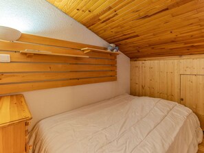 Quarto com cabeceira em ripas de madeira, cama com edredom branco e uma pequena prateleira com um ursinho de pelúcia.