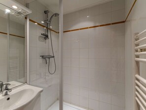 Casa de banho com cabine de duche em vidro, lavatório branco e espelho.