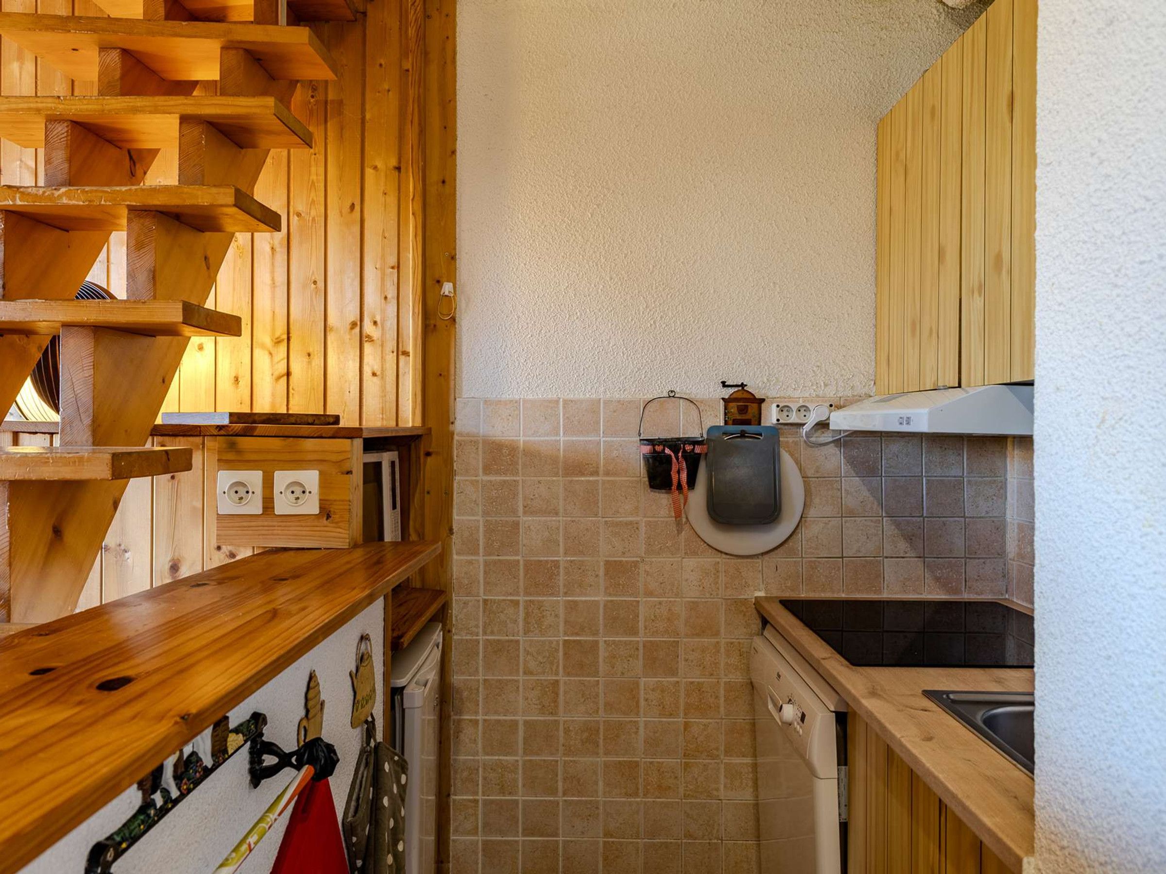 Cozinha compacta com prateleiras de madeira, painel de azulejos e lava-louças embutida.