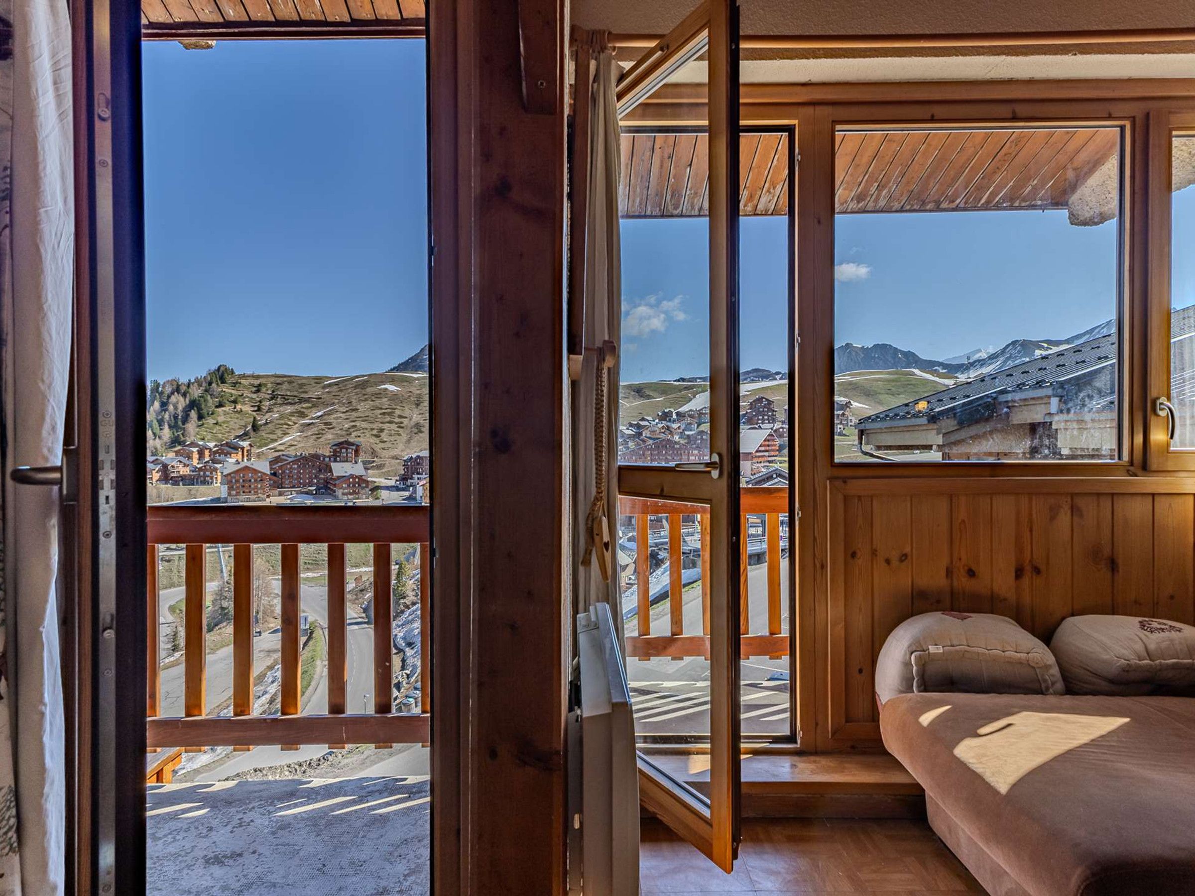 Ein Zimmer mit Holzbalkon, einem Bett mit Kissen und Blick auf eine Stadt und Berge.