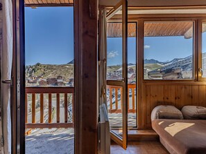 Ein Zimmer mit Holzbalkon, einem Bett mit Kissen und Blick auf eine Stadt und Berge.