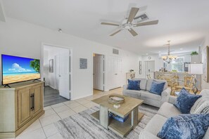 A living room with a television, a ceiling fan, and a dining area with a table and chairs. - Olde Marco Inn Unit 208 | Walk To Food, Shops & More (Marco Island)