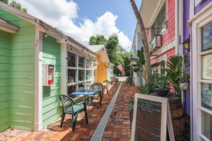 A narrow alleyway with colorful buildings, a brick pathway, outdoor seating, and a signboard. - Olde Marco Inn Unit 208 | Walk To Food, Shops & More (Marco Island)