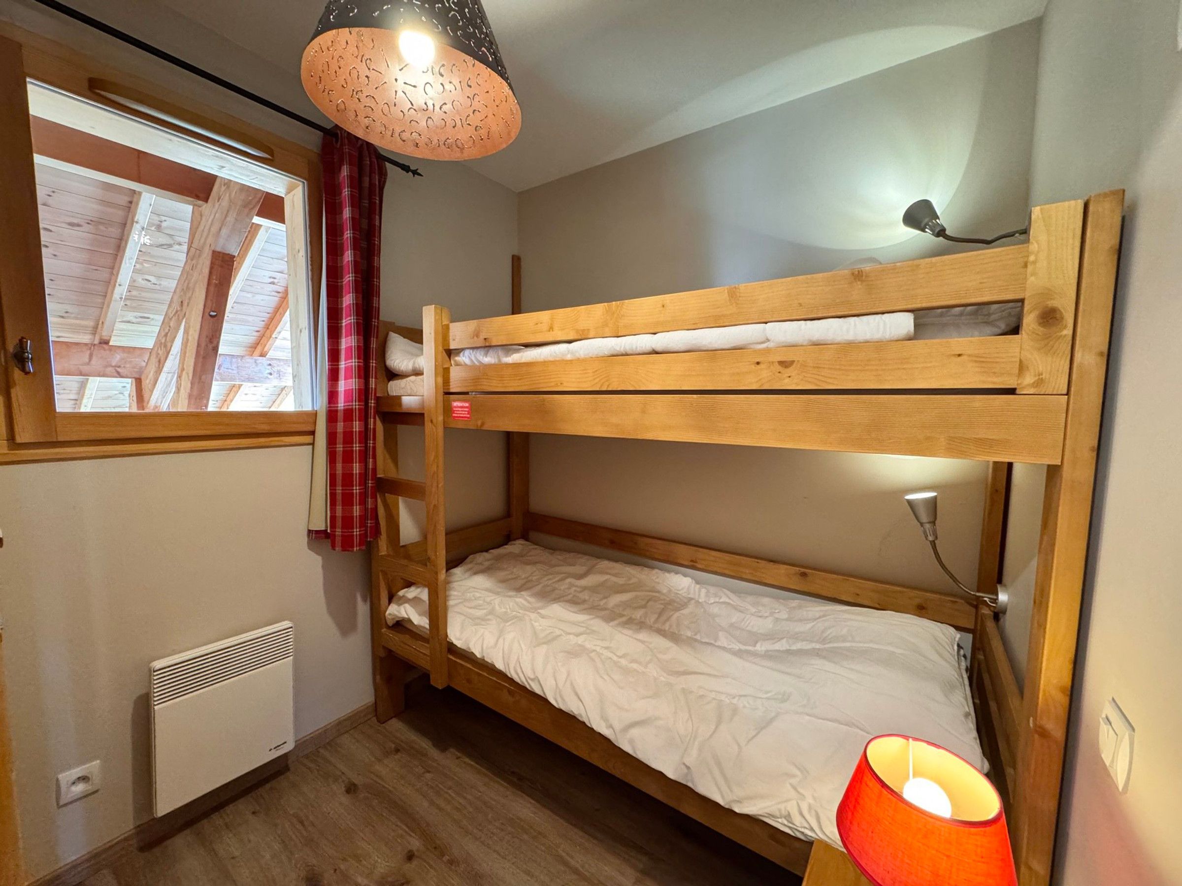 Habitación con literas, una ventana, un radiador y una lámpara colgante.