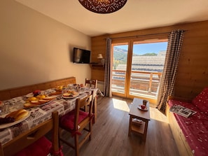 Une pièce avec une table à manger dressée pour le petit-déjeuner, un canapé, une petite table avec une tasse, et une vue sur un bâtiment traditionnel par la fenêtre.