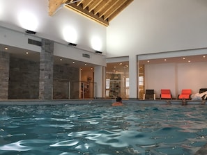 Une piscine intérieure à l’eau claire, avec un mur en pierre et une rambarde en verre.