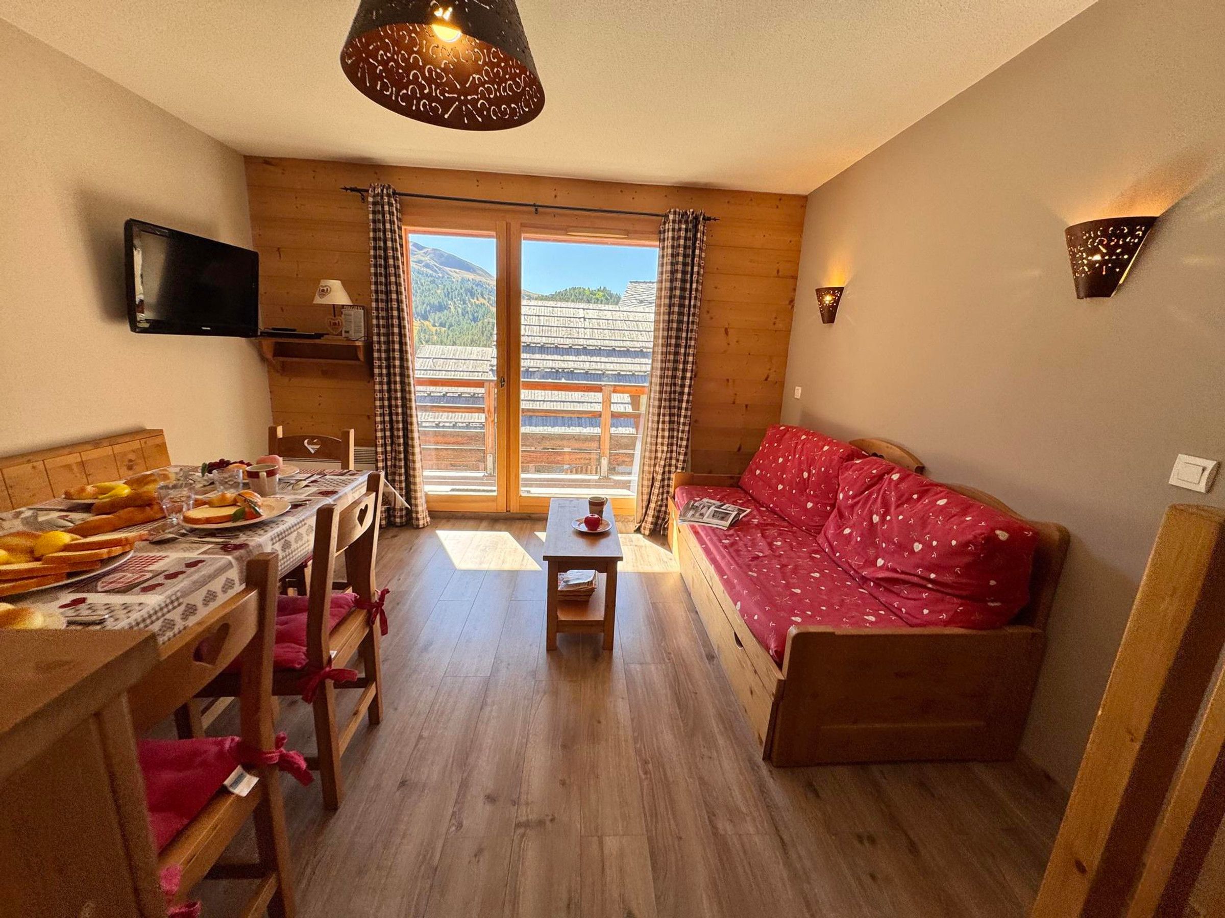 Una habitación acogedora con una mesa de madera dispuesta para el desayuno, un sofá y un televisor montado en la pared.