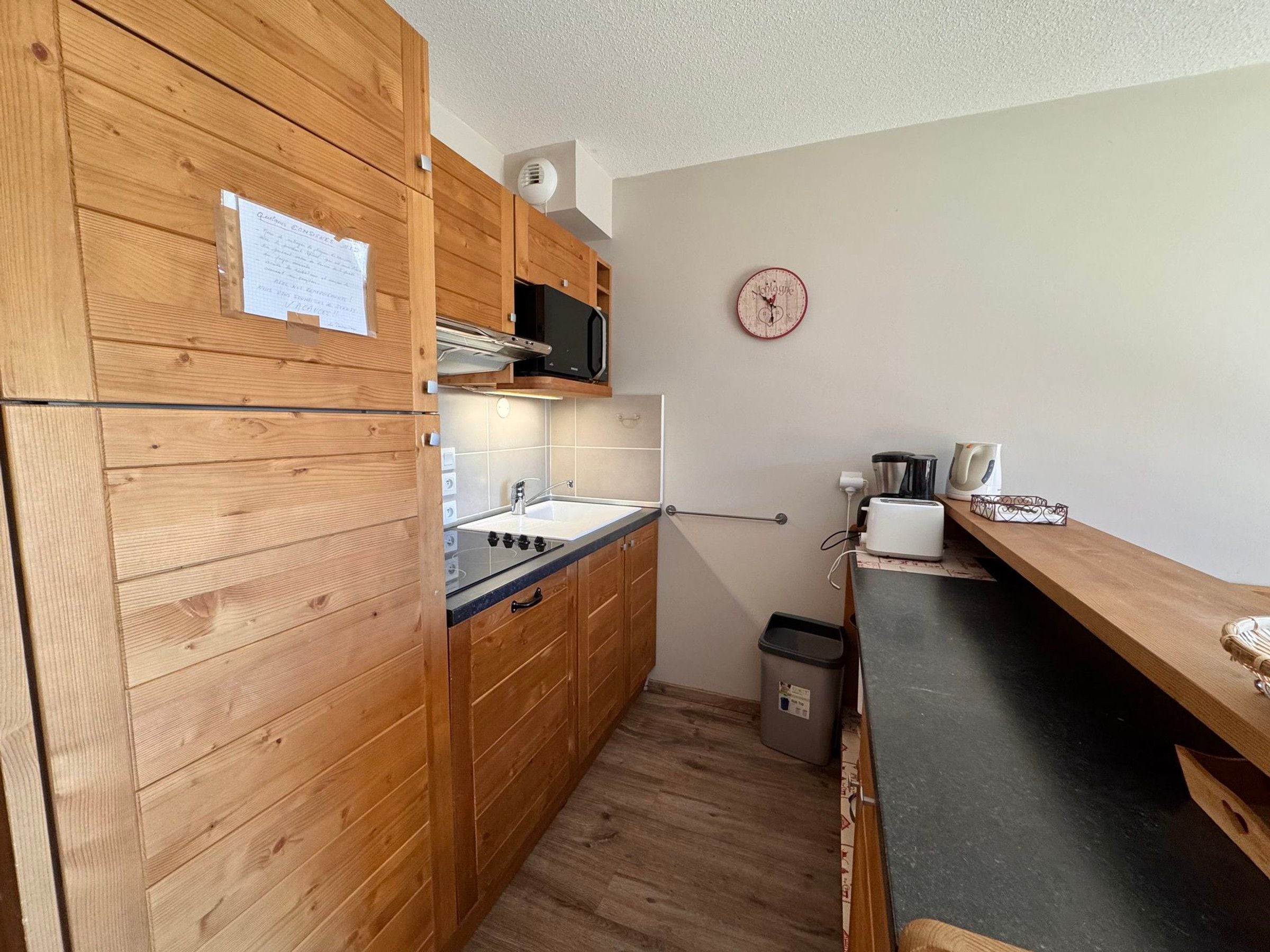 Una cocina compacta con armarios de madera, microondas, lavamanos y tostadora.