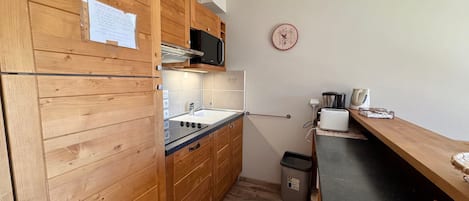 A compact kitchen with wooden cabinets, a microwave, a sink, and a toaster.