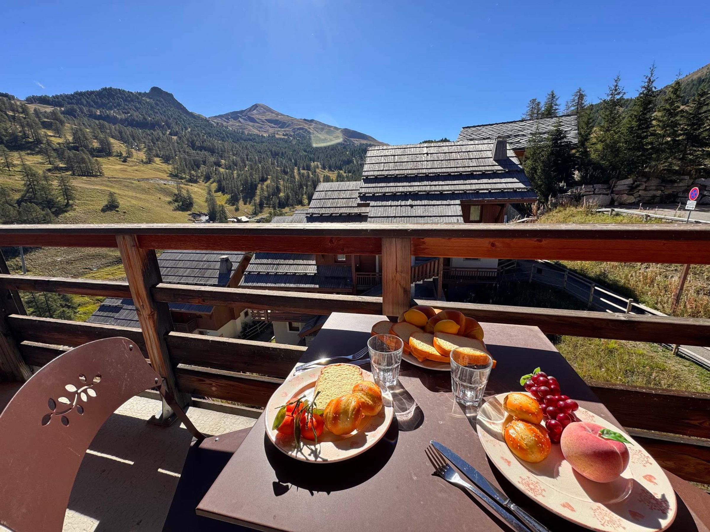 Una mesa de comedor con platos de comida y vasos, frente a un paisaje montañoso y un edificio de madera.