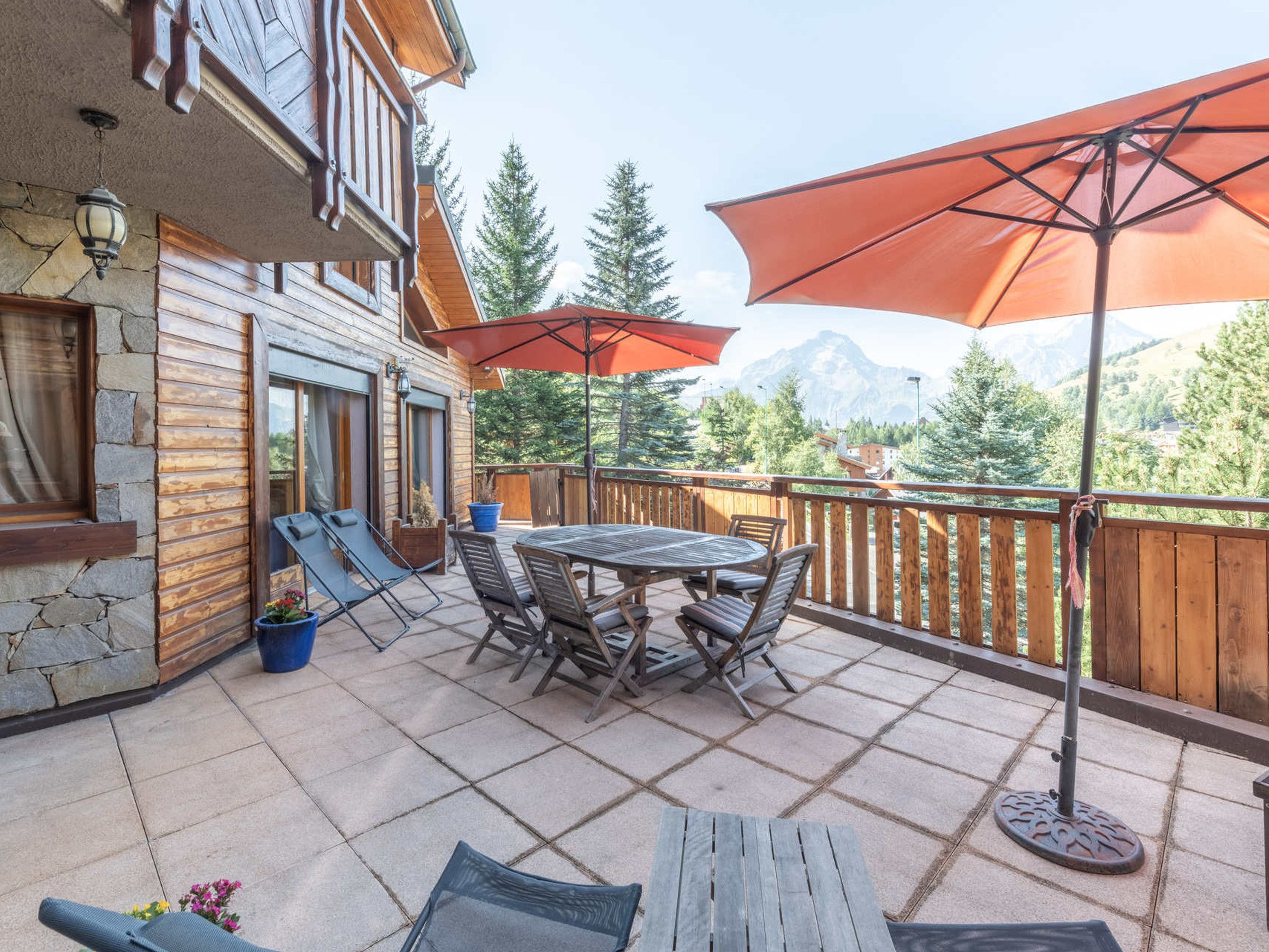 Une terrasse en bois avec une table et des chaises, un fauteuil de relaxation et un grand parasol.