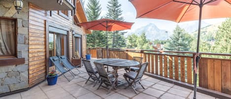 Une terrasse en bois avec une table et des chaises, un fauteuil de relaxation et un grand parasol.
