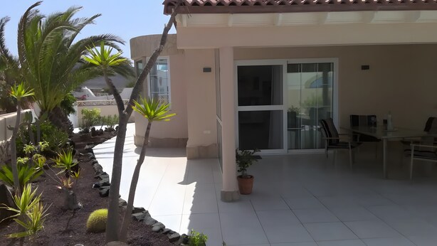 Un patio cubierto con comedor, una puerta de vidrio que da a una habitación y diversas plantas.