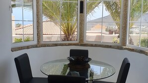 Una habitación con una mesa y sillas de vidrio, una pared de piedra y vistas a palmeras y edificios afuera.