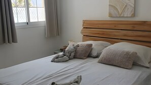 Ein Schlafzimmer mit einem hölzernen Kopfteil, einem Bett mit weißer Bettwäsche und einem Fenster mit Vorhängen.