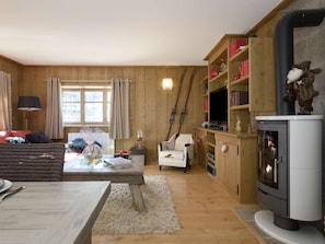 Un salon chaleureux avec un décor intérieur en bois, une cheminée, un téléviseur et un coin repas comprenant une table et des chaises.