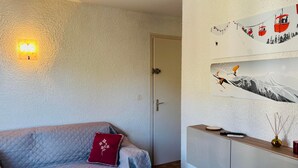 Ett rum med en soffa, en vägglampa och en vägg prydd med ett konstverk med skidmotiv.