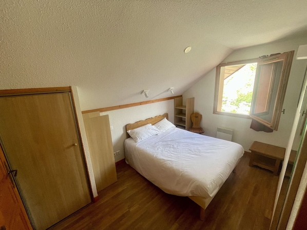 Een slaapkamer met een enkel bed, een houten garderobe, een klein nachtkastje en een raam met uitzicht op groen.