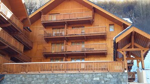 A multi-story wooden building with balconies, a stone base, and a wooden deck. - Convenient apartment, pets allowed - 6 guests (Valloire)
