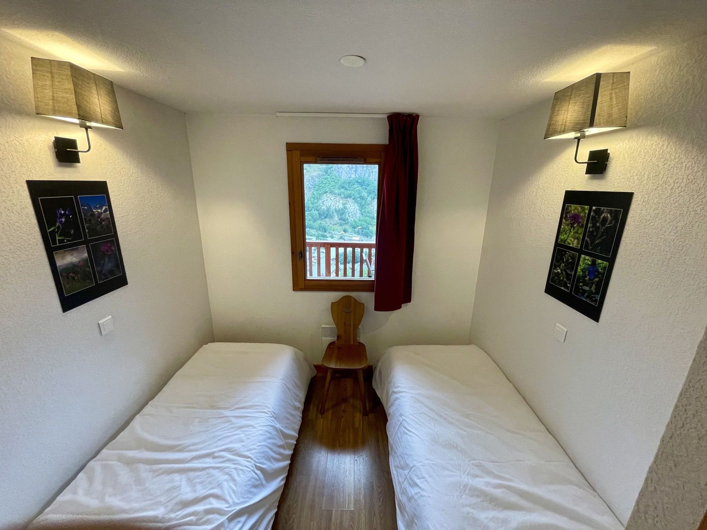 Een kamer met twee eenpersoonsbedden, een raam met uitzicht op groen en wandlampen.