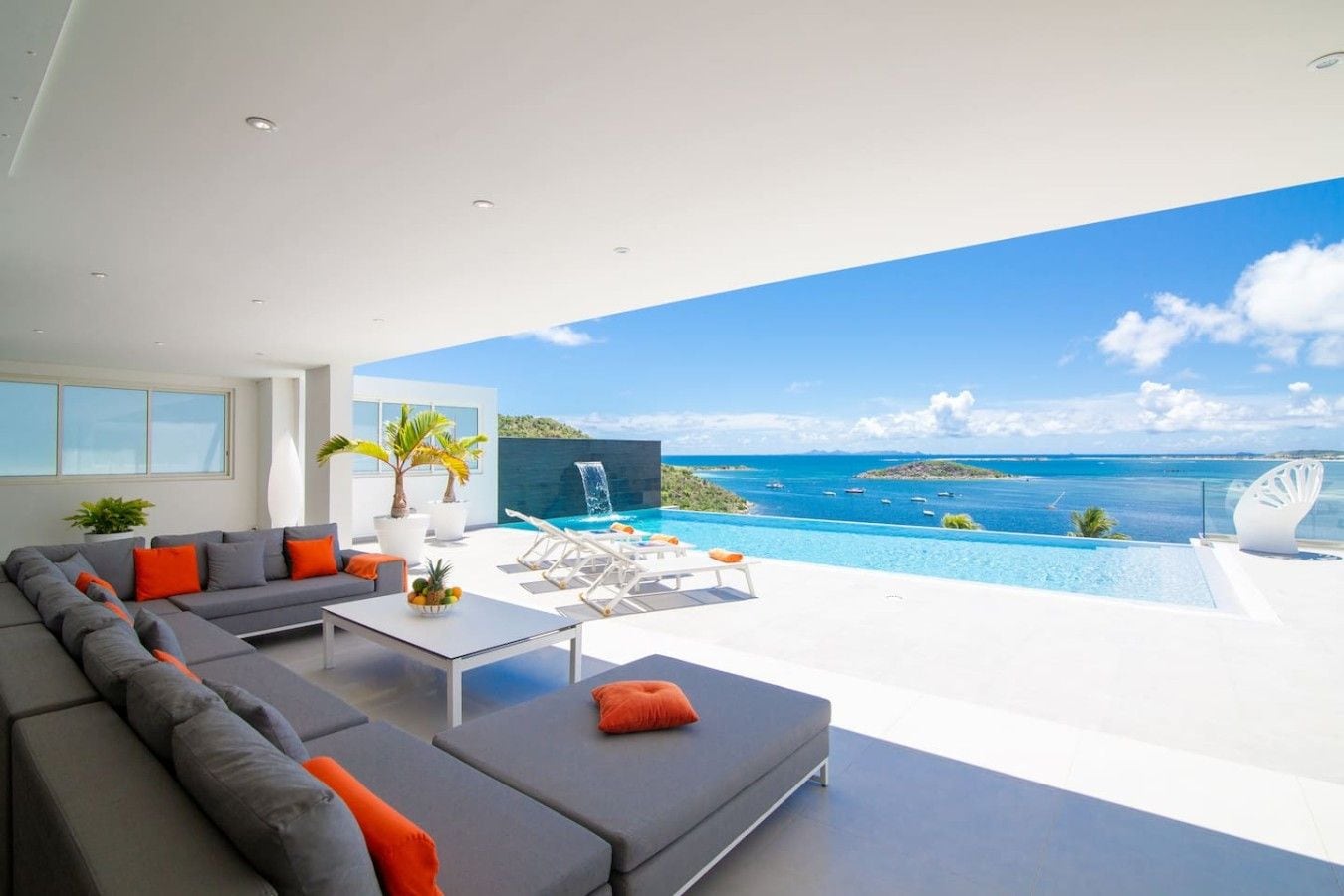 A modern living room with a large gray sectional sofa, a coffee table, and a view of a private pool and ocean.