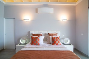 A bedroom with a bed, two bedside lamps, a wall-mounted air conditioner, and a door. - Villa Magnolia Forever Luxe and Exception (St Martin)