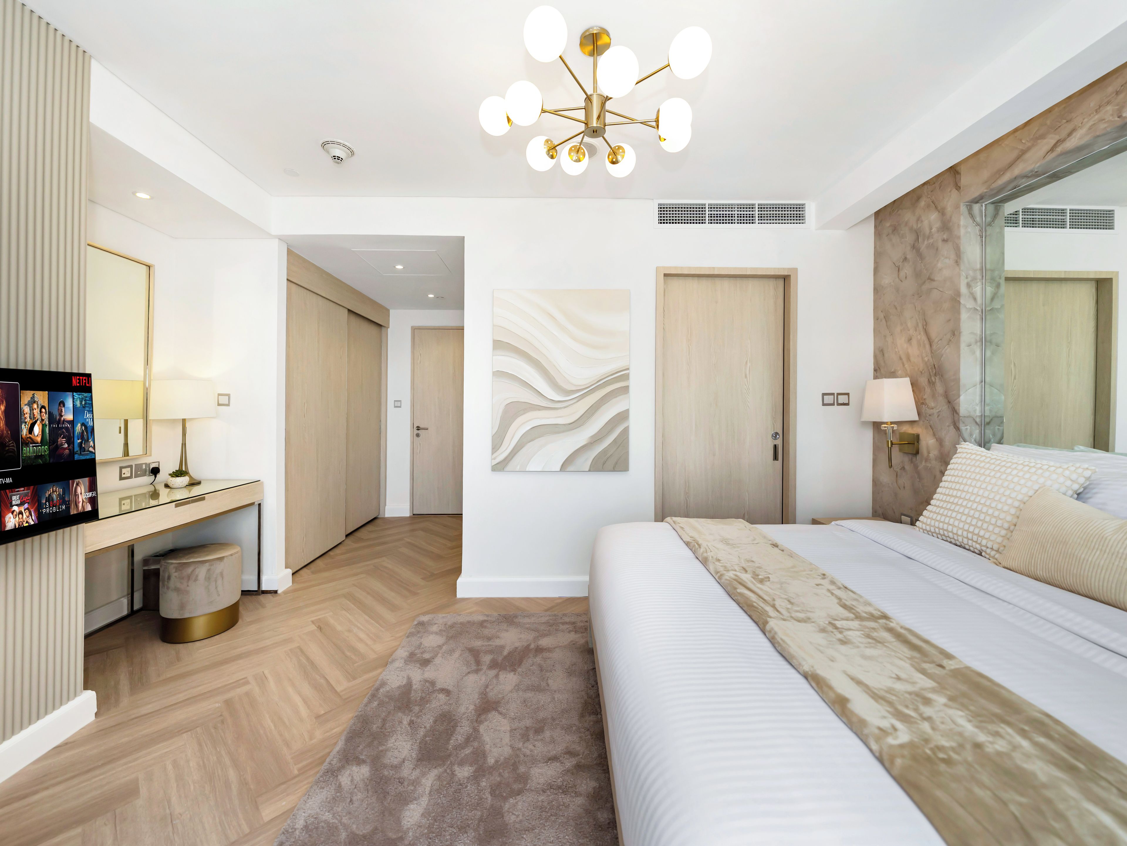 Habitación de hotel moderna con una cama grande, un escritorio con televisor, una lámpara de pared y un adorno en la pared.