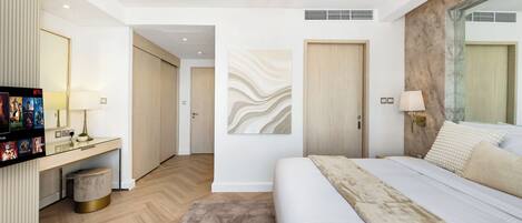A modern hotel room with a large bed, a desk with a TV, a wall-mounted lamp, and a decorative wall piece.