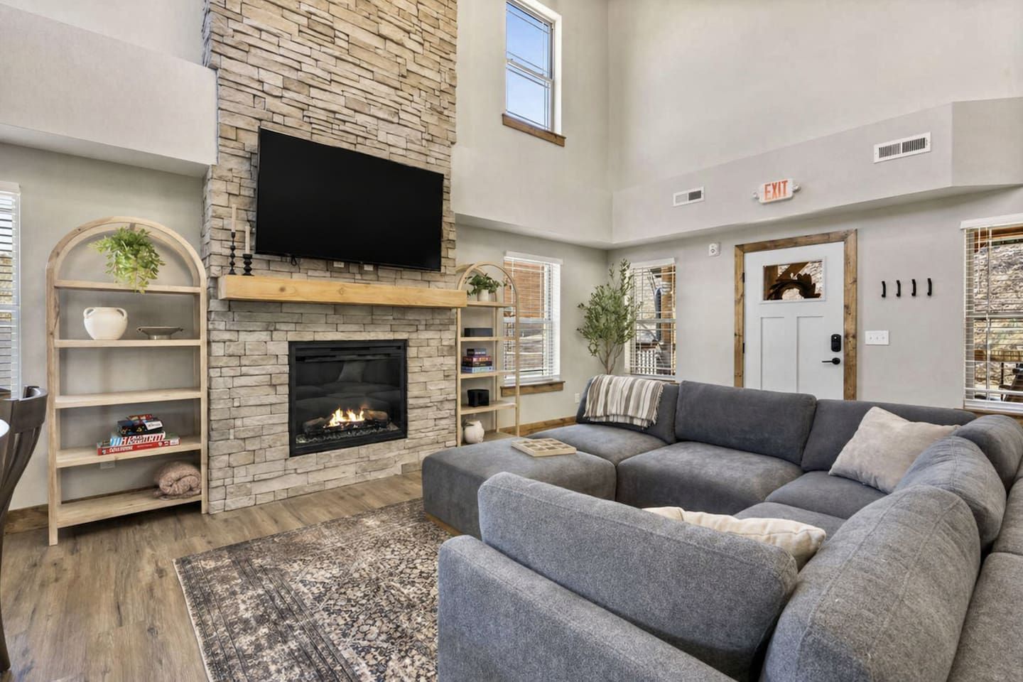 A living room with a stone fireplace, a grey sofa, and a flat-screen TV mounted above the fireplace.