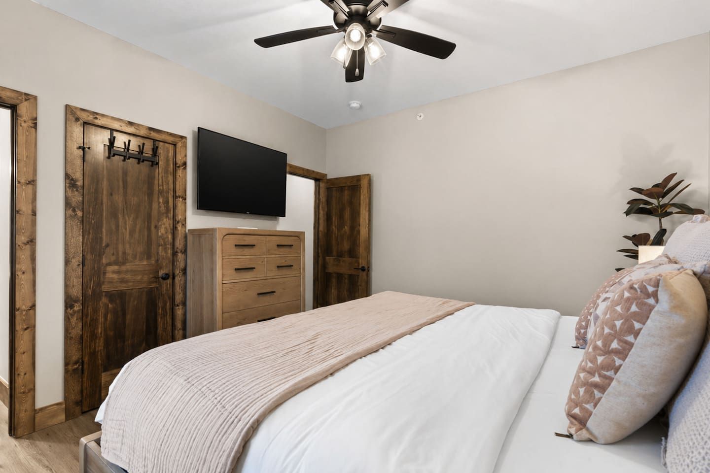 Une chambre à coucher avec un lit, un ventilateur de plafond, une télévision, des portes en bois et une commode.