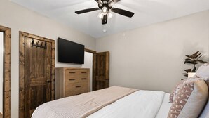 Une chambre à coucher avec un lit, un ventilateur de plafond, une télévision, des portes en bois et une commode.