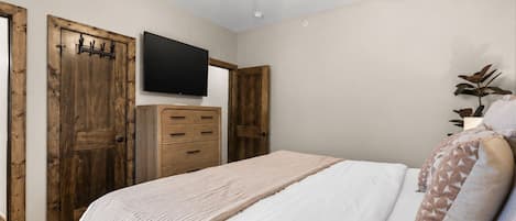 Une chambre à coucher avec un lit, un ventilateur de plafond, une télévision, des portes en bois et une commode.