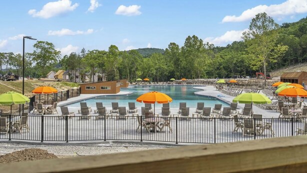 Une piscine entourée d’une clôture et d’arbres, avec des chaises longues et des parasols.