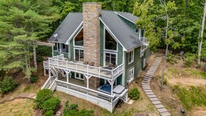 A two-story house with a stone chimney, a balcony, and a deck. - Woodland Dreams by Carolina Mornings | Hot Tub, Fire Pit, & Mtn Views Near AVL (Swannanoa)