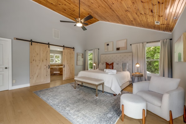 Um quarto espaçoso com uma cama grande, um banco, um sofá e um ventilador de teto.