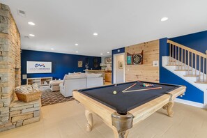 Uma sala de estar moderna com mesa de bilhar, sofá e área de cozinha.
