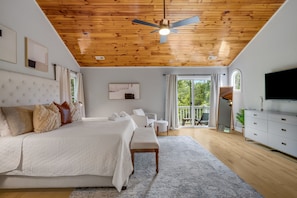 Quarto com cama, mesas de cabeceira, ventilador de teto, uma janela grande e vista para o exterior.