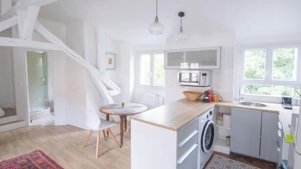A modern kitchen with a washing machine, a microwave, and a dining area with a table and chairs. - A CLASSIC FRENCH CHARACTER WITH A FRESH, CONTEMPORARY INTERIOR. (Paris)