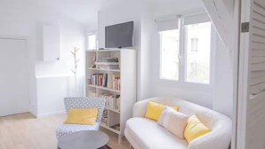 A living room with a white sofa, a small round table, a bookshelf, and a television. - A CLASSIC FRENCH CHARACTER WITH A FRESH, CONTEMPORARY INTERIOR. (Paris)