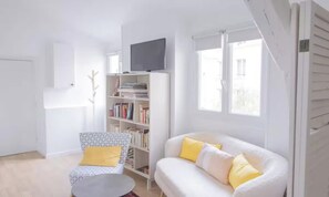 A living room with a white sofa, a small round table, a bookshelf, and a television. - SPACIOUS RENOVATED STUDIO IN THE HEART OF PARIS (Paris)