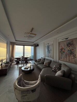 Ein modernes Wohnzimmer mit einer großen Couch, einem Esstisch und Blick aufs Meer.