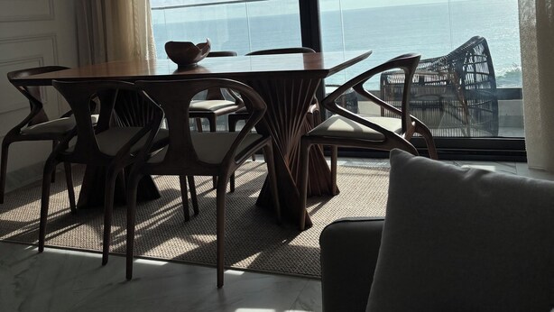 Quarto moderno com mesa de jantar e cadeiras, sofá e uma grande janela com vista para o mar.